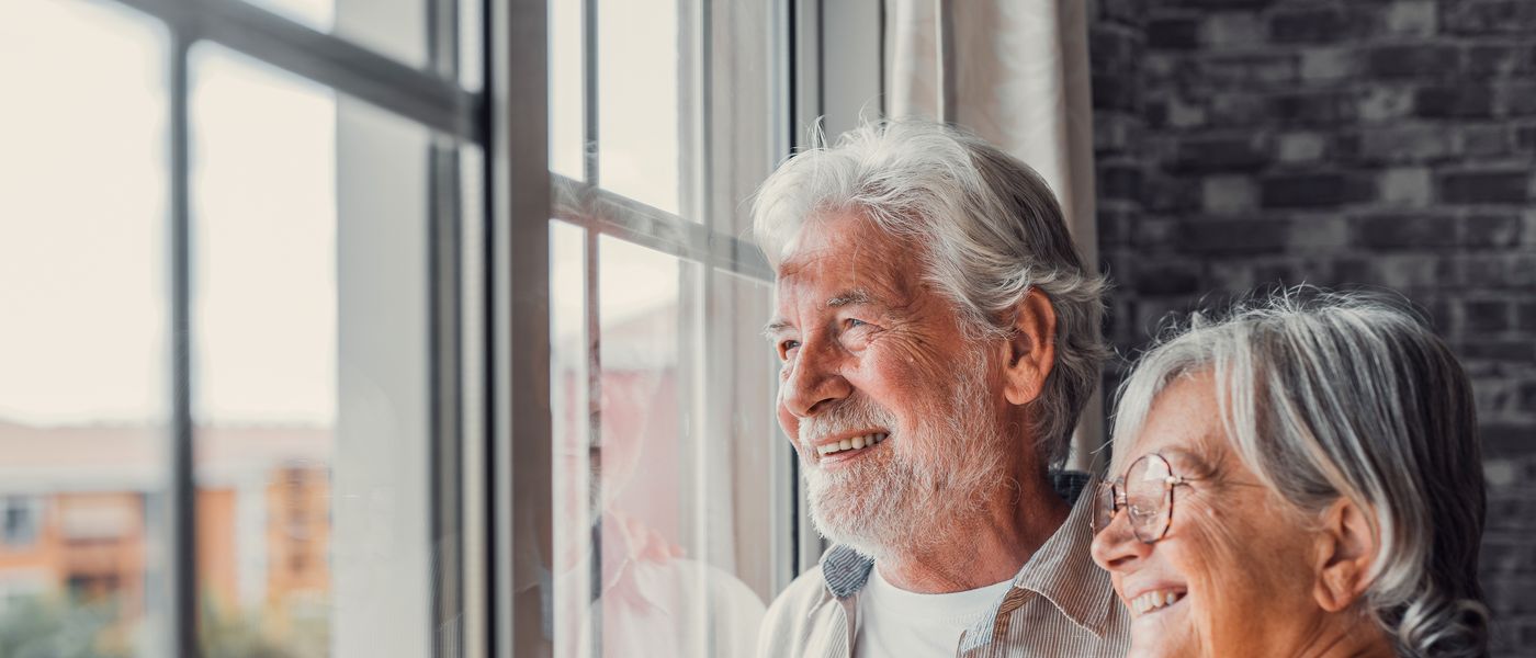 Retired couple looking out of the window of their home